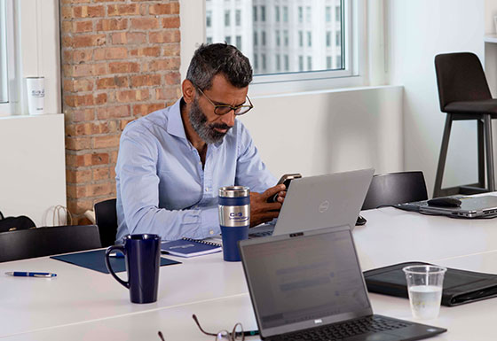 Male employee works diligently on laptop and mobile device during a break from a group meeting